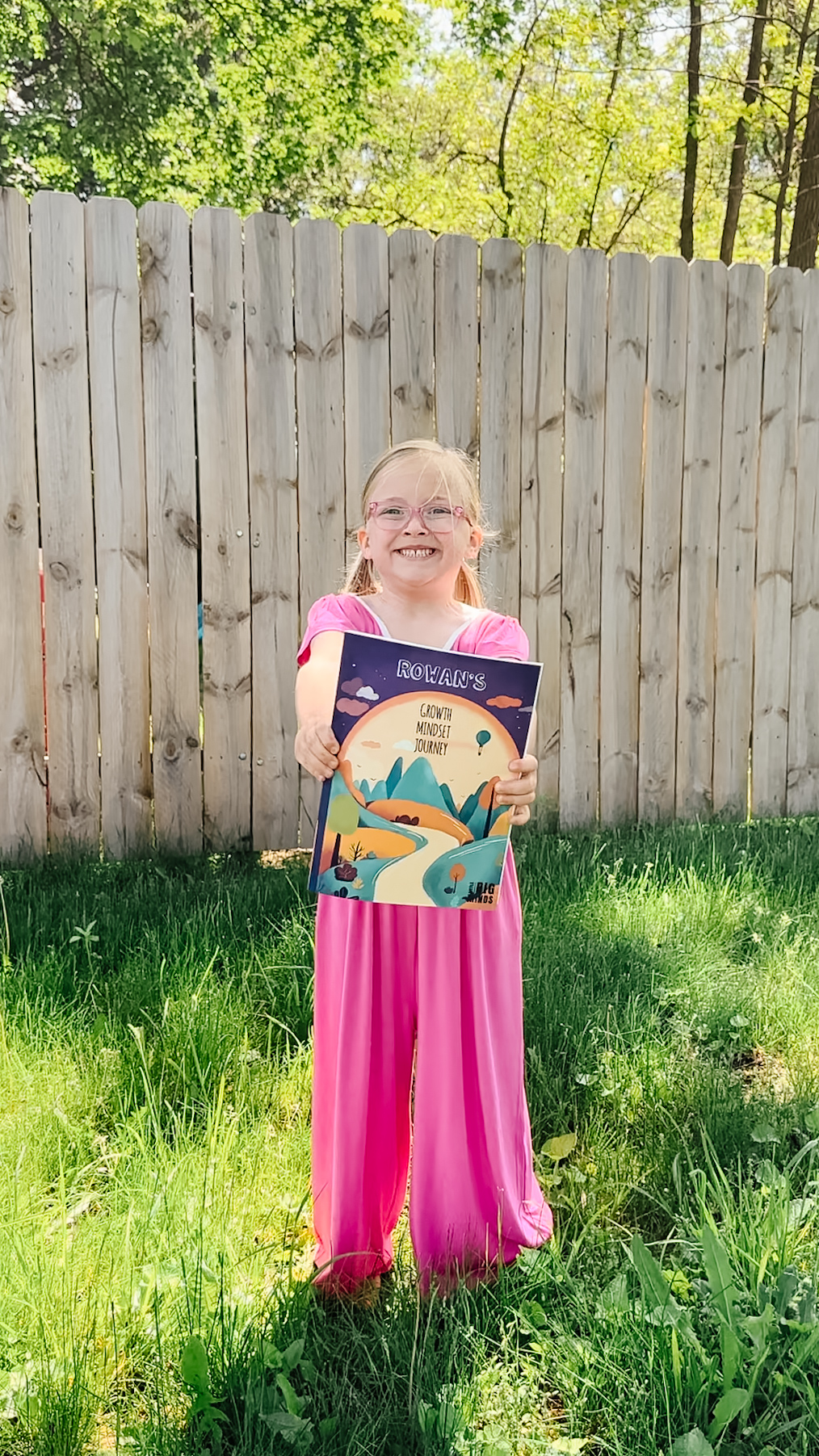 Girl proudly holding personalized book cover outside — name visible